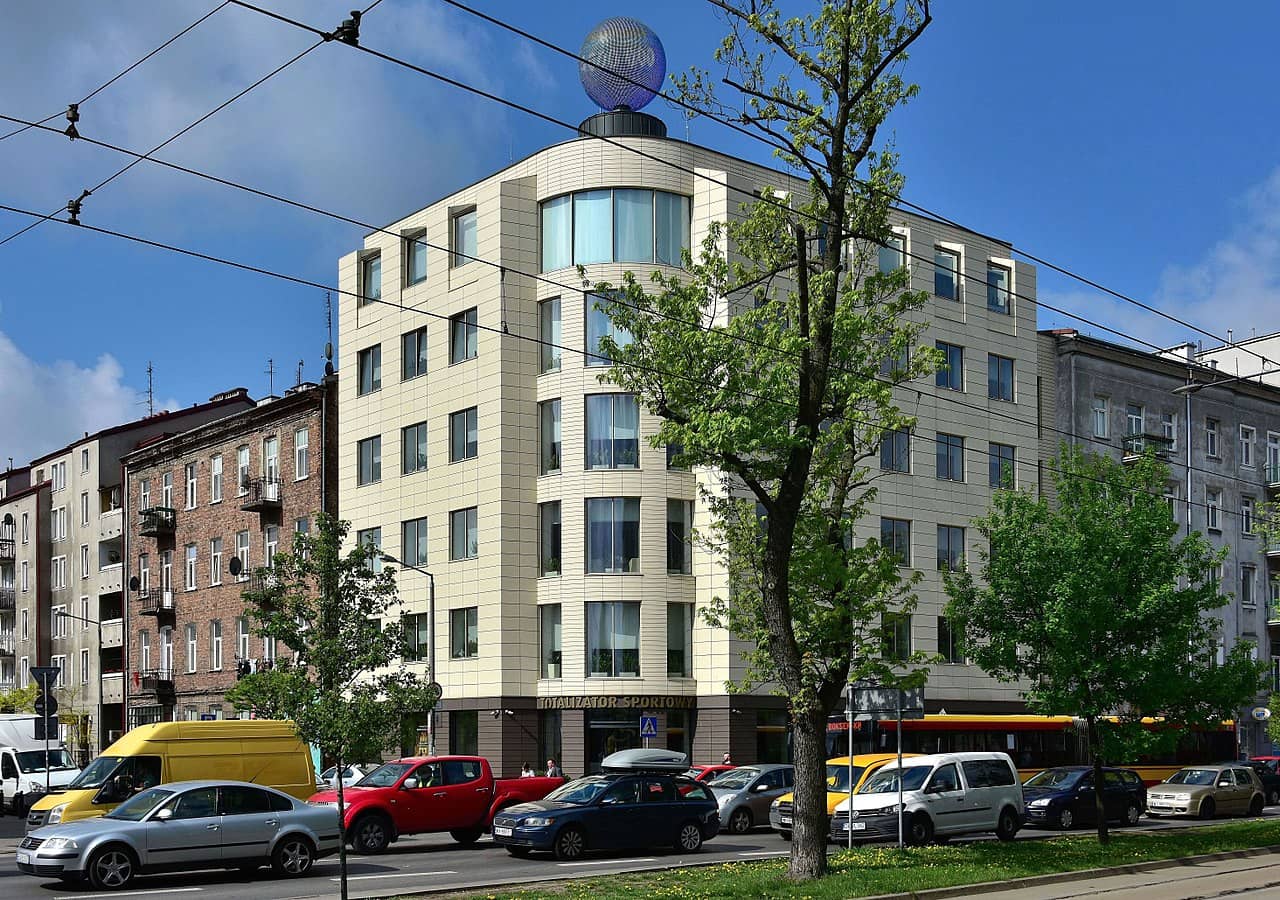 widok na budynek spółki Totalizator Sportowy w Warszawie, na pierwszym planie drzewo i ulica pełna samochodów