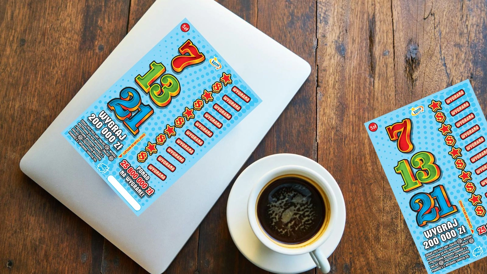 zdrapki Lotto 7 13 21, srebrny laptop, filiżanka z kawą, spodek, na brązowym blacie stołu