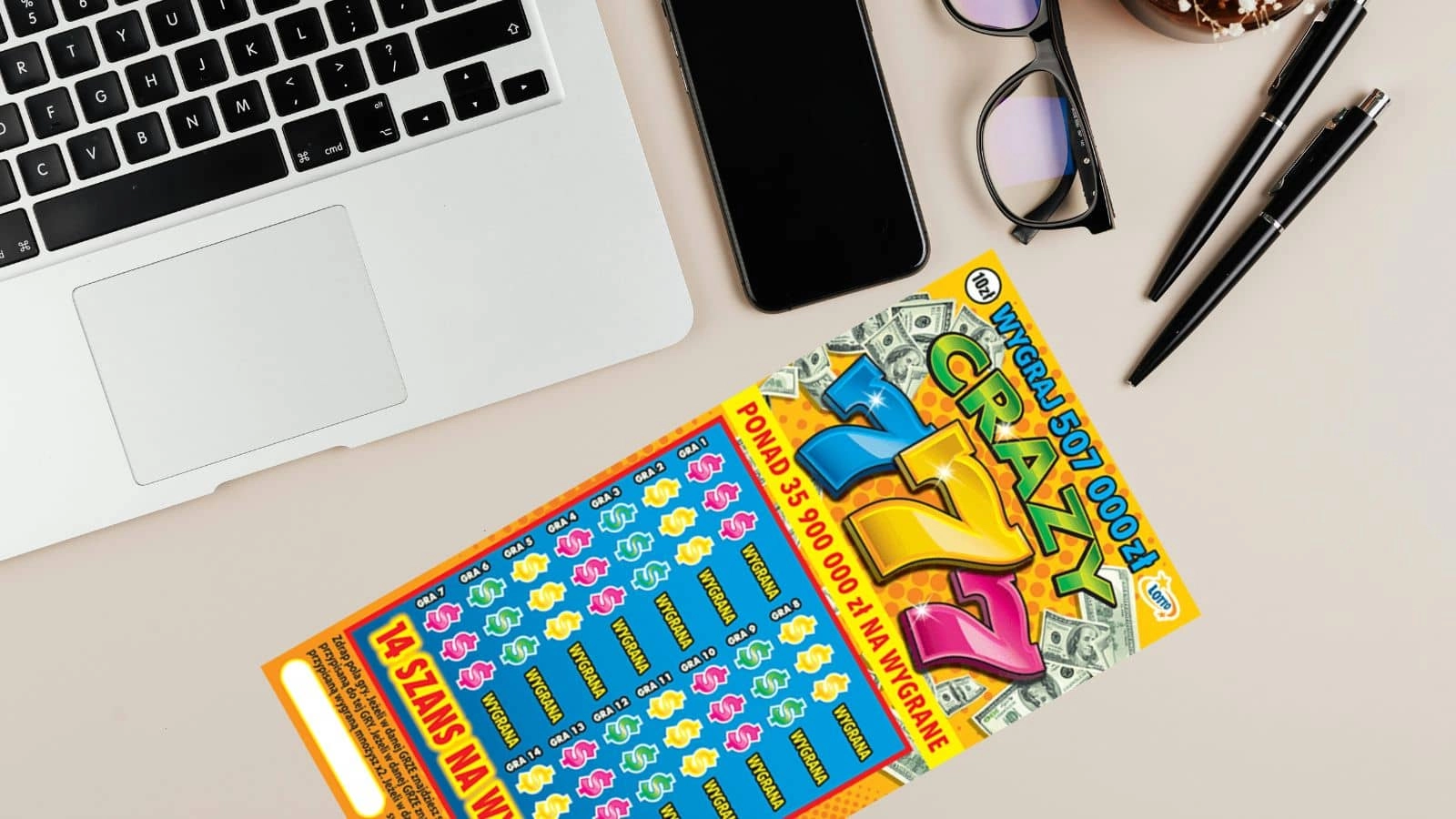 zdrapka lotto, laptop, telefon, okulary i długopis na beżowym blacie stołu