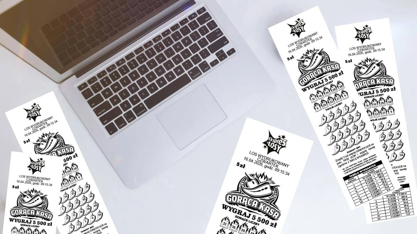 otwarty macbook oraz losy gry Gorąca Kasa (0017) na białym blacie biurka