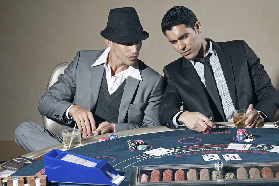 dwaj mężczyźni w garniturach grający w pokera przy stole w kasynie