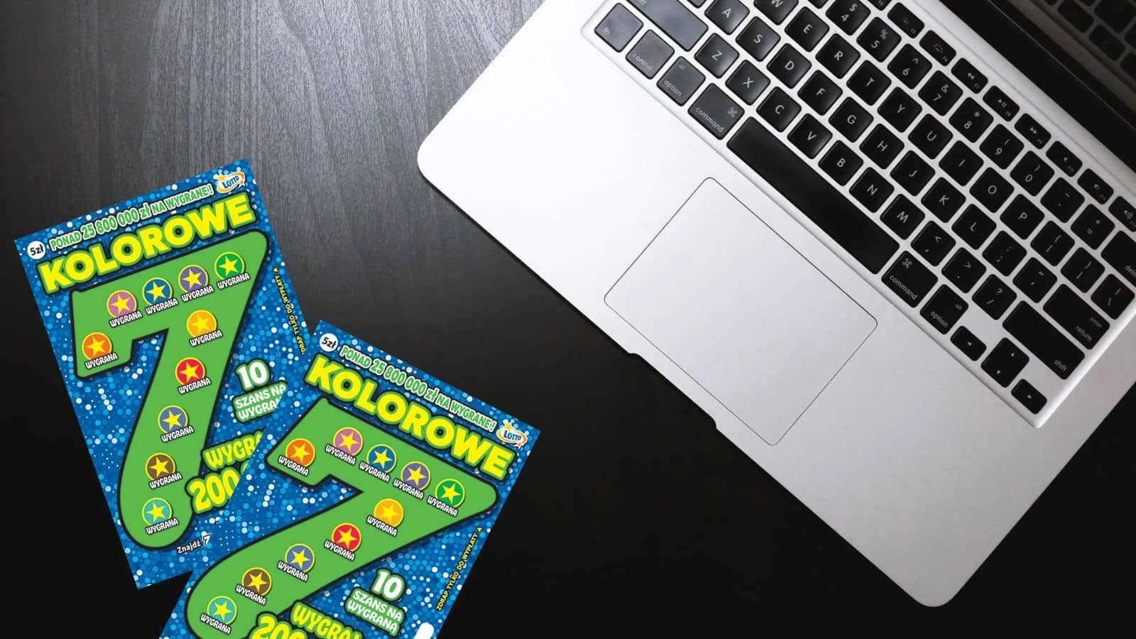 zdrapki lotto Kolorowe 7 oraz klawiatura laptopa na czarnym blacie stołu