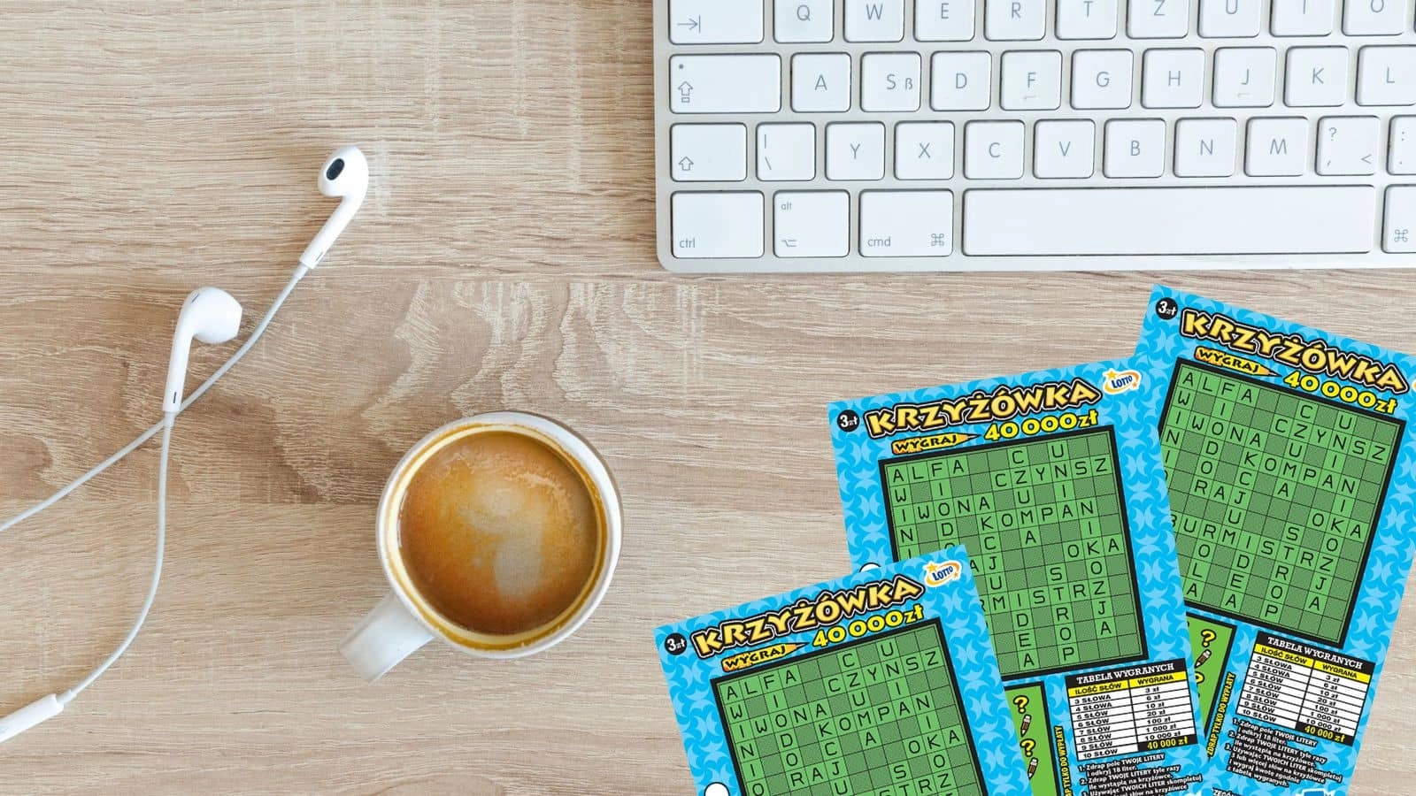 słuchawki douszne, biała klawiatura, kubek kawy, zdrapki lotto Krzyżówka na jasno drewnianym tle, widok z góry