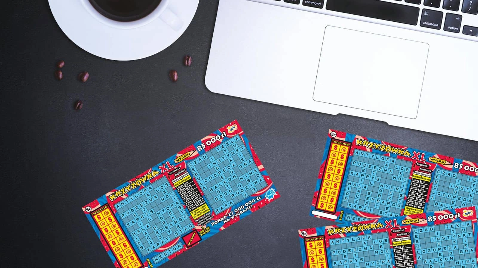 zdrapki lotto krzyżówka xl, filiżnaka z kawą, ziarna kawy, laptop na chropowatym czarnym blacie biurka