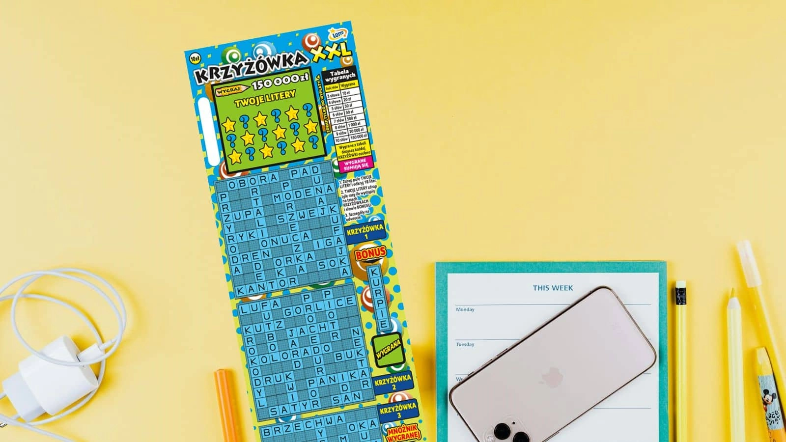 ładowarka, ołówek, zdrapka lotto, notes i iphone na żółtym tle
