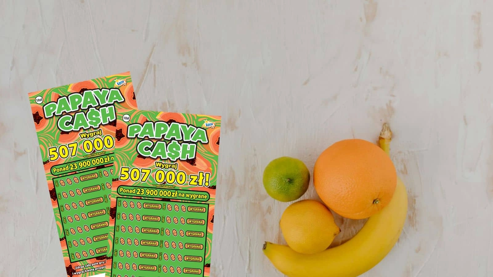zdrapki lotto Papaya Cash, owoce: limonka, pomarańcza, cytryna, banan na nierówno pomalowanym na biało blacie stołu