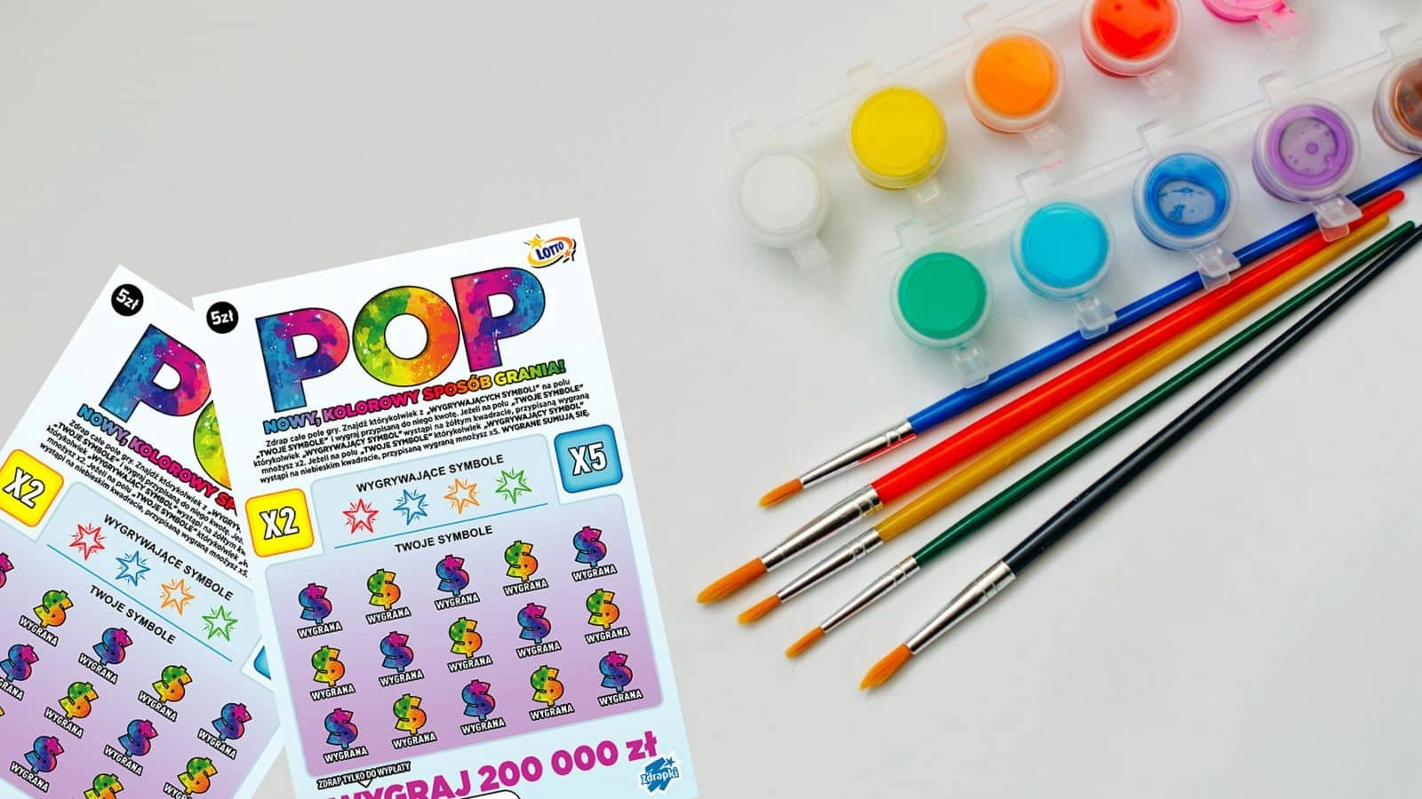 zdrapki Lotto POP oraz farbki do malowania w różnych kolorach i pędzłe na białym blacie stołu