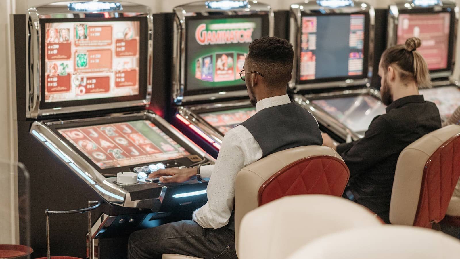 dwóch mężczyzn siedzi przy automatach w salonie gier Lotto