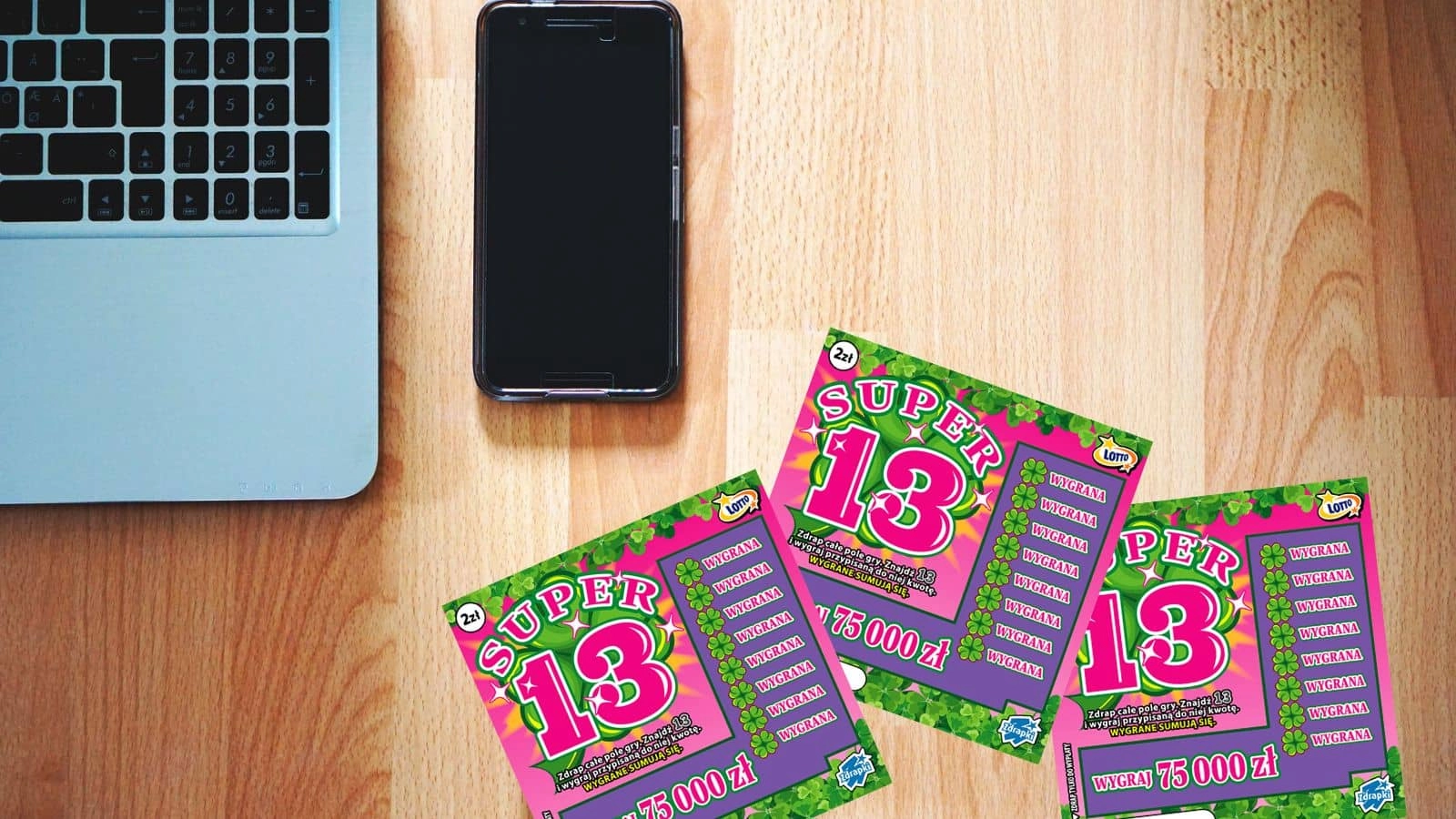 fragment laptopa, smartfon oraz zdrapki lotto super 13 na jasno drewnianych panelach podłogowych, widok z góry