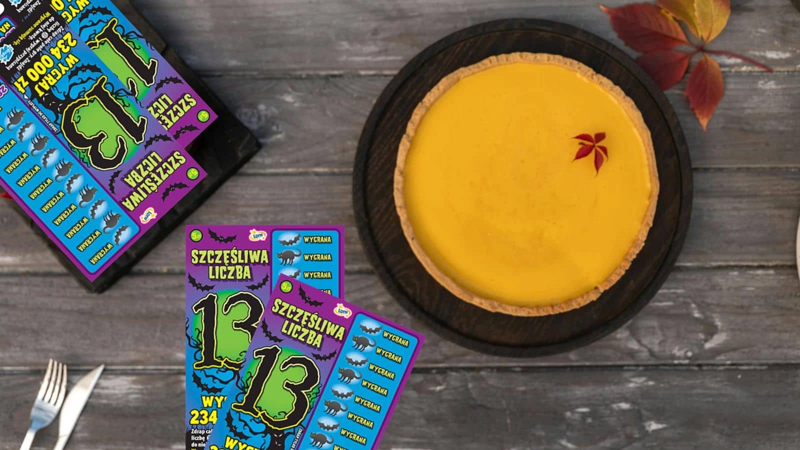 jesienny drewniany stolik, zdrapki lotto halloweenowe, sztucce, zupa dyniowa, liść klonu