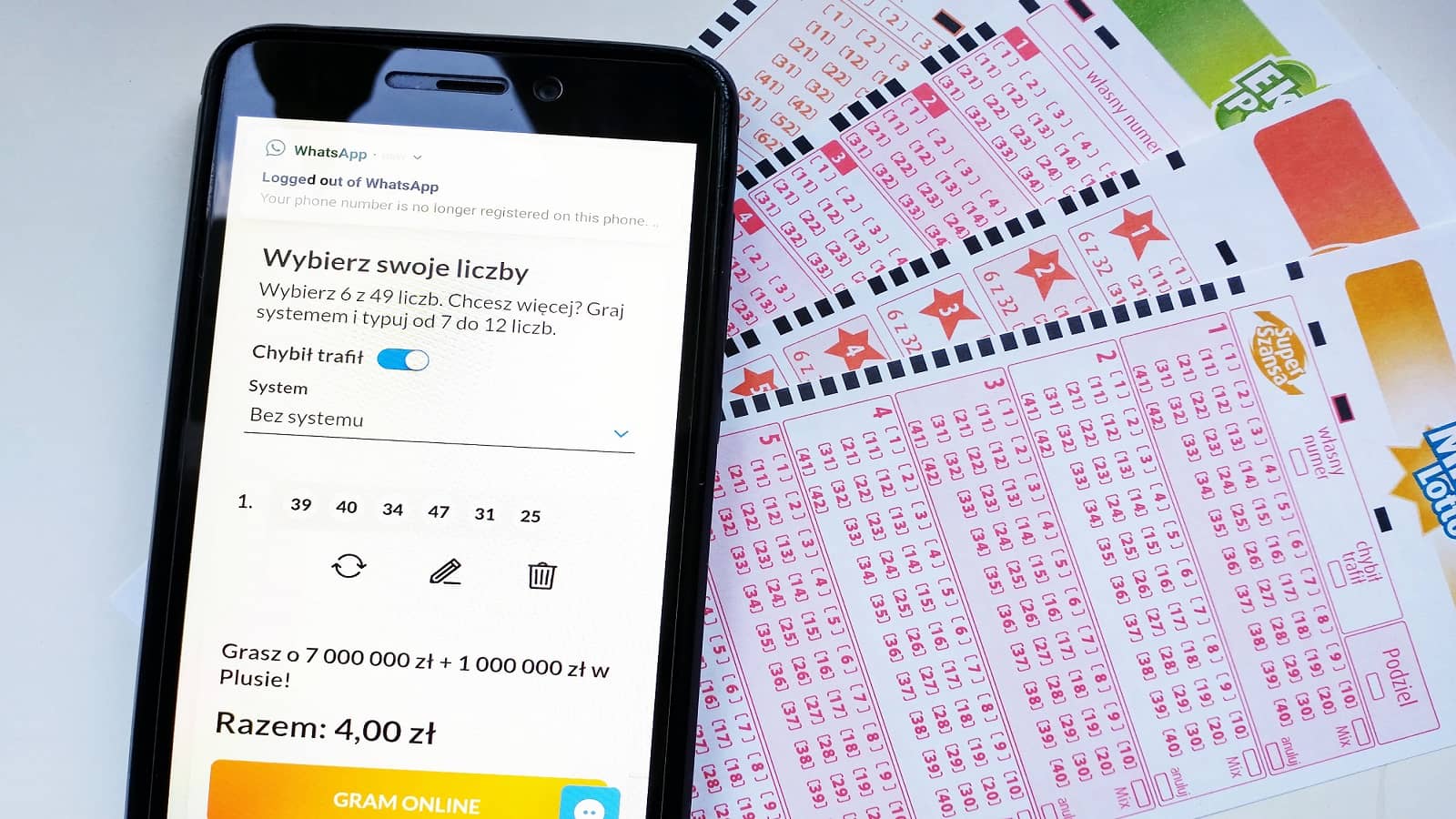 telefon z włączoną aplikacją Lotto online oraz obok kupony Lotto, położone na stole
