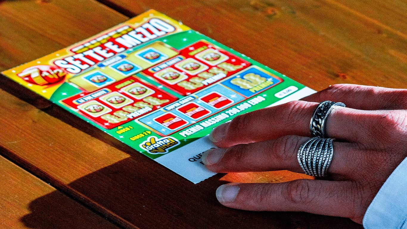 kobieca ręka trzymająca zdrapkę Lotto na drewnianym stole